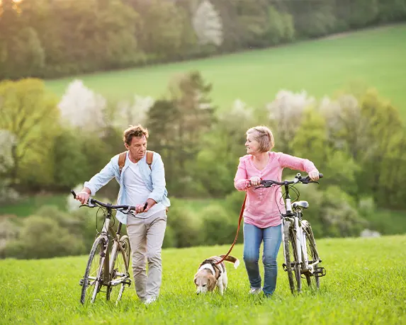 couple walking alongside their bikes in a grassy field with their dog index annuities