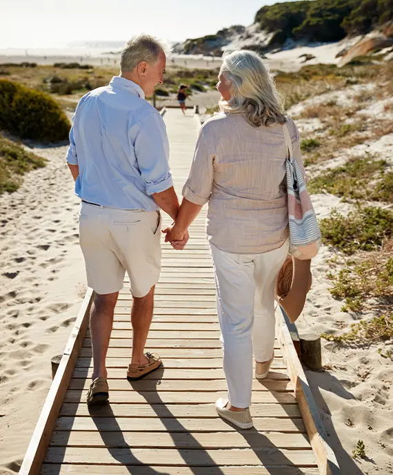 retired couple holding hands while they walk on a board walk toward the beach rate of return